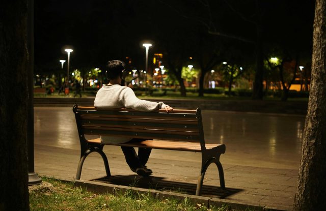 Person sitting on bench looking out over city landscape at night.